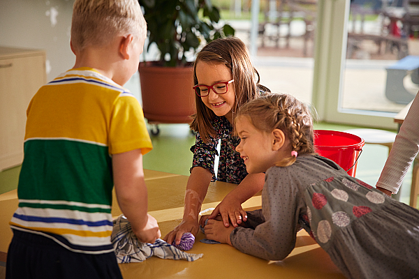 Kinder wischen gemeinsam einen Tisch in ihrer Kita ab.