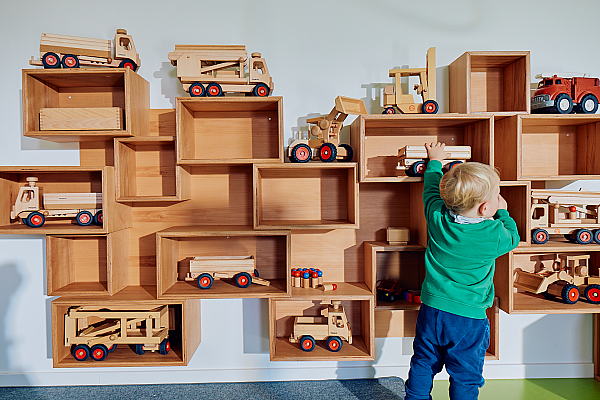 Ein Kind steht vor einem Holzregal mit Spielsachen
