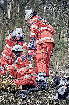 Drei Mitglieder der Rettungshundestaffel versorgen einen gerade durch den Rettungshund gefunden Mann im Wald.