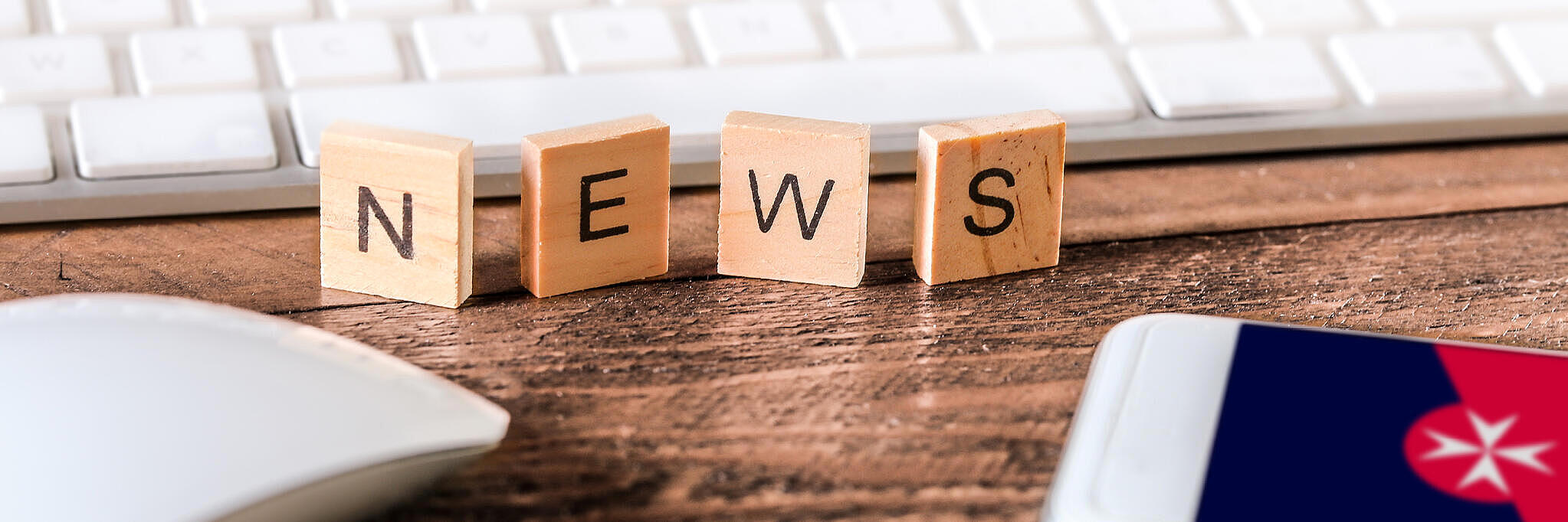 Holzbuchstaben, die das Wort "News" bilden, stehen vor einer weißen Tastatur