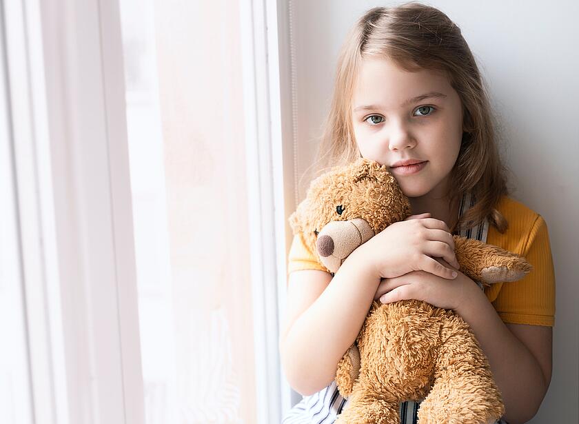 Mädchen hält einen Teddybären am Fenster.