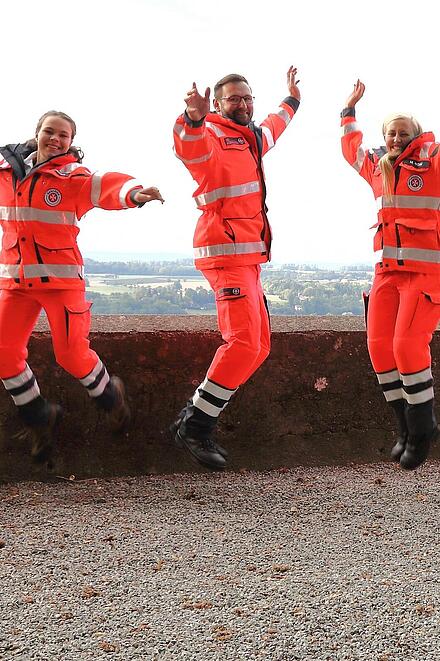 mehrere Johanniter in Einsatzkleidung hüpfen fröhlich in die Luft