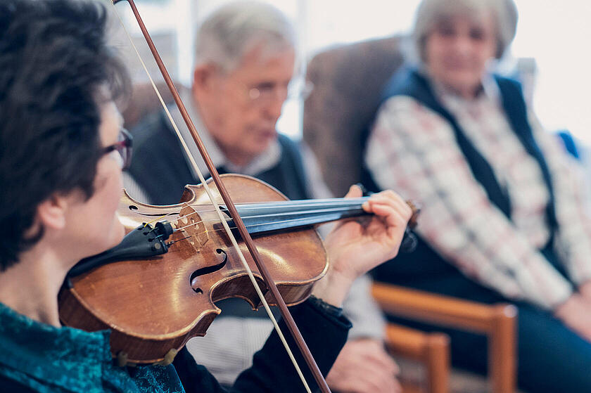 Zwei Bewohnende lauschen einer Violinistin beim Konzert