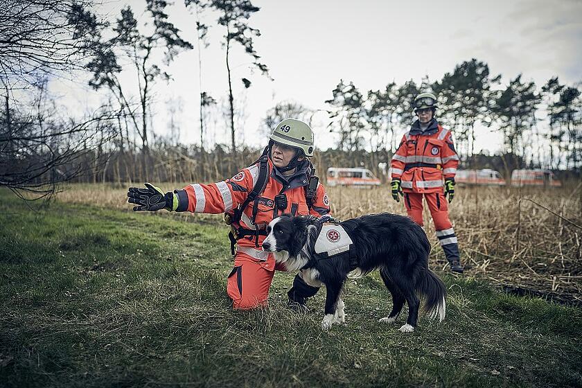 Zwei Einsatzkräfte der Rettungshundestaffel mit einem Rettungshund im Wald