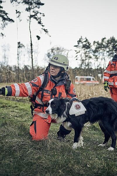 Zwei Einsatzkräfte der Rettungshundestaffel mit einem Rettungshund im Wald