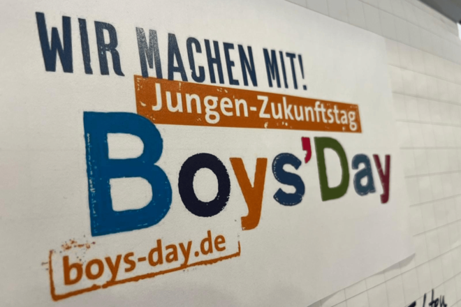 Plakat mit Schriftzug "Boys'Day" an einer weißen Wand.