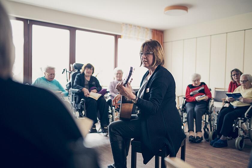 Eine Mitarbeiterin spielt Gitarre und singt mit den Bewohnern
