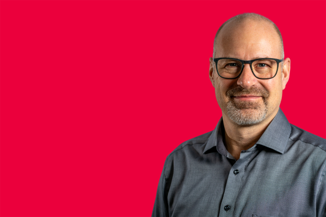 Portrait eines Mitarbeiters vor rotem Hintergrund
