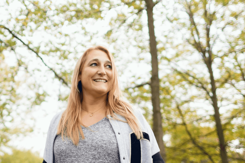 Eine Frau in einer Parkanlage. Sie hat lange rötliche-blonde Haare und blickt seitlich vom Fotografen weg. 