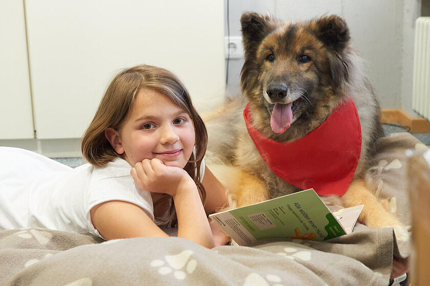 Ein Mädchen liest einem Johanniter-Leshund aus ihrem Buch vor.
