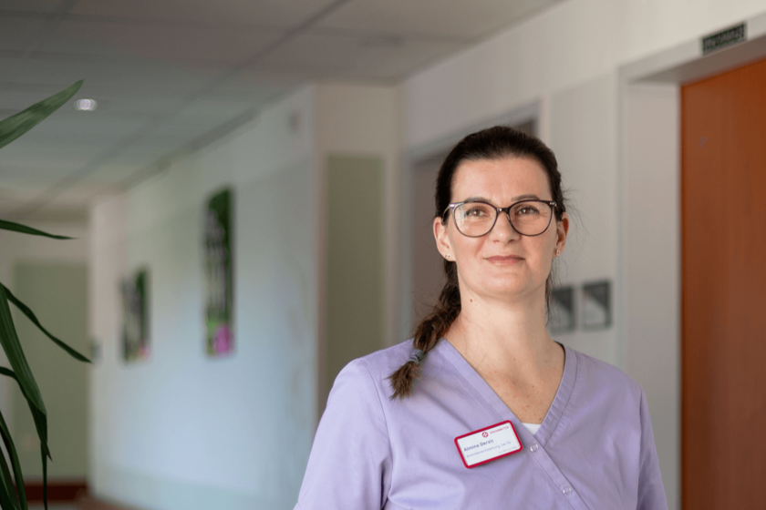 Frau im Flur eines Pflegeheims, trägt Arbeitskleidung und Namensschild.
