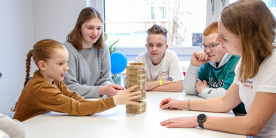 Jugendliche sitzen um einen Tisch und spielen Jenga als Teamspiel in der Pause.