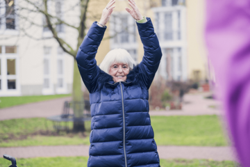 Eine Dame in einer blauen Jacke macht Sport in einer Gruppe