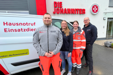 Vier Mitarbeitende aus dem Johanniter-Hausnotruf stehen aufgereiht vor einem Johanniter-Fahrzeug - das wiederum vor der Johanniter-Regionalgeschäftsstelle steht. Das Gebäude trägt das Johanniter-Logo über dem Eingang.