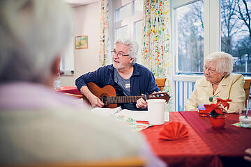 Ein Mitarbeiter spielt Gitarre und eine Gruppe von Bewohnenden hört zu