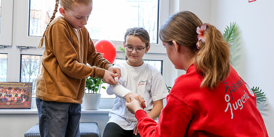 Kinder der Johanniter-Jugend üben das Anlegen eines Verbands am Unterarm.