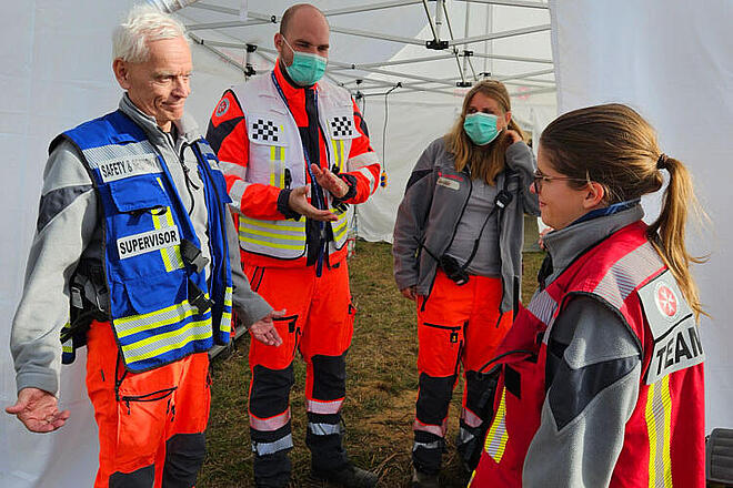 Vier Mitglieder des EMTs der Johanniter stehen vor einem Behandlungszelt. 