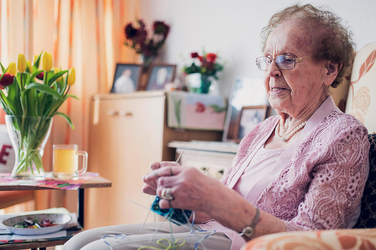 Dame mit Strickzeug im Sessel im Bewohnerzimmer