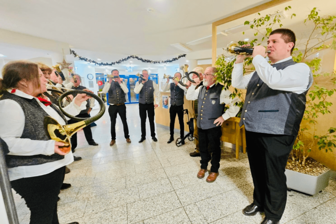Bläsergruppe in Tracht spielt Jagdhorn in einer geschmückten Halle, Bläserinnen und Bläser stehen im Halbkreis.