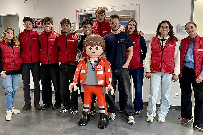 Jugendliche der Johanniter suchen neue Fördermitglieder und werben für unsere sozialen Projekte. Gemeinsam haben sie mit der großen Plastikplaymobilfigur ein Foto gemacht. Sie lachen fröhlich in die Kamera.