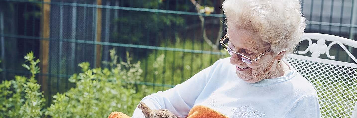 Eine Bewohnerin sitzt im Garten und streichelt Kaninchen