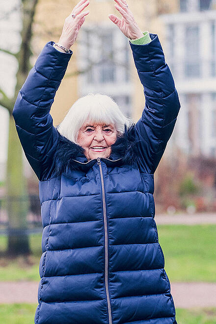 Eine Damen in einer blauen Jacke macht Sport in einer Gruppe