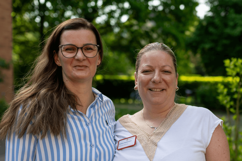Zwei Frauen lächeln gemeinsam in einem Garten, Porträtaufnahme.  