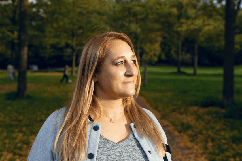 Eine Frau in einer Parkanlage. Sie hat lange rötliche-blonde Haare und blickt seitlich vom Fotografen weg. 