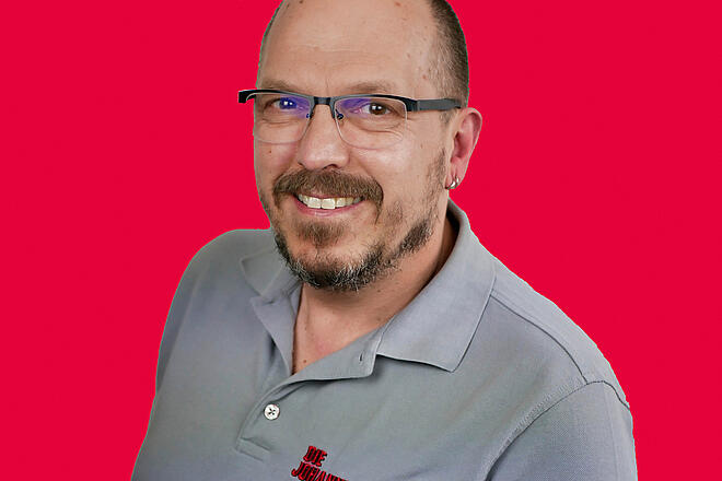 Portrait eines Mitarbeiters vor rotem Hintergrund