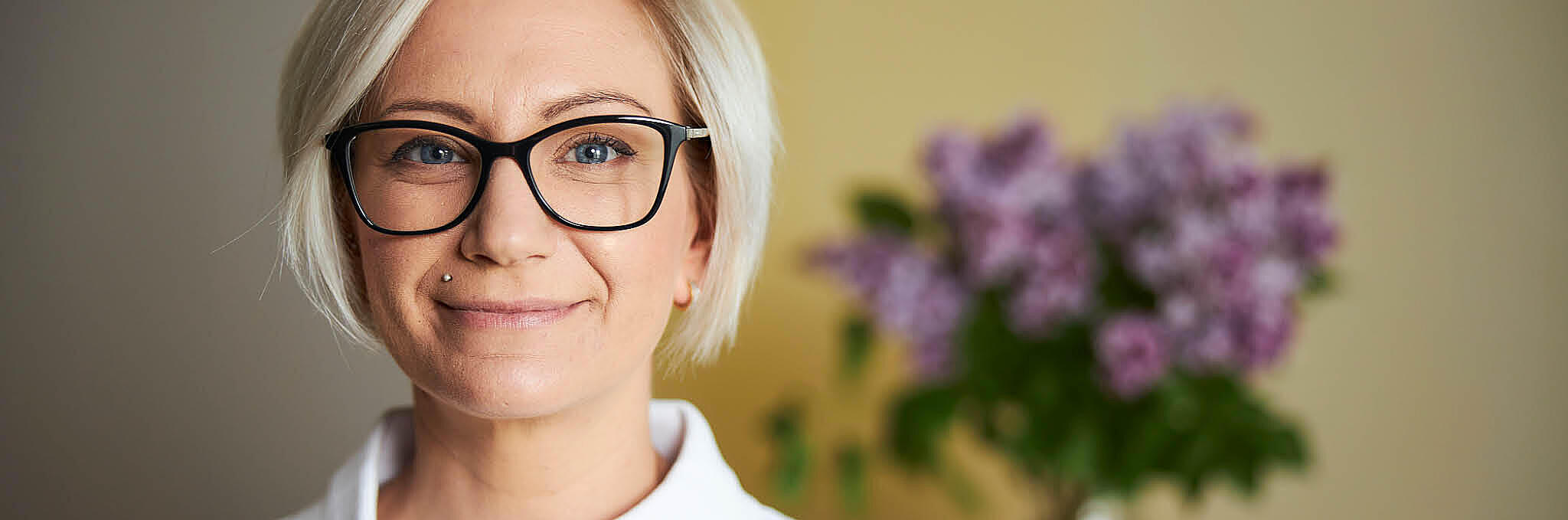 Eine Frau mit Brille steht vor einer gelben Wand