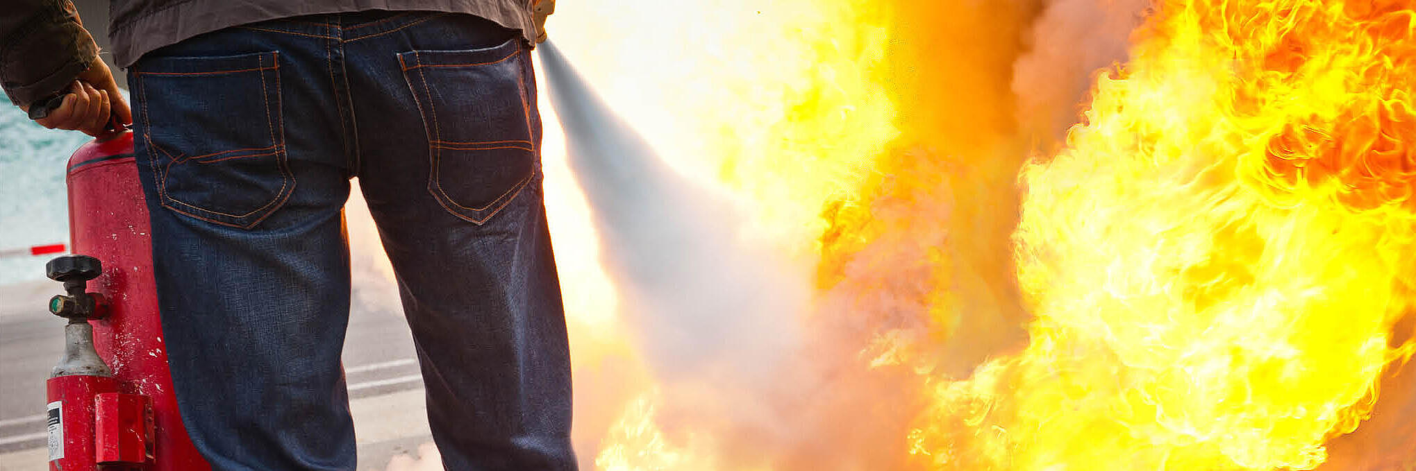 Eine Person hält einen Feuerlöscher in der Hand und löscht einen Brand