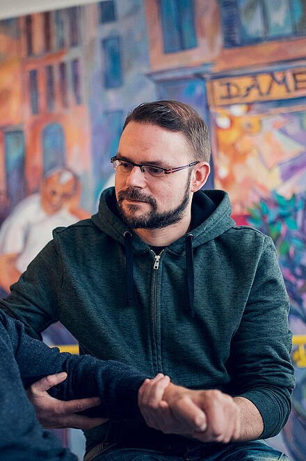 Ein jüngerer Mann im blauen Pullover hilft einem Bewohner des Johanniter-Haus Empelde