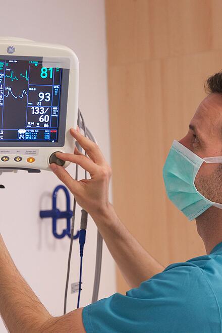 Pflegekraft mit Mundschutz stellt Patientenmonitor ein.