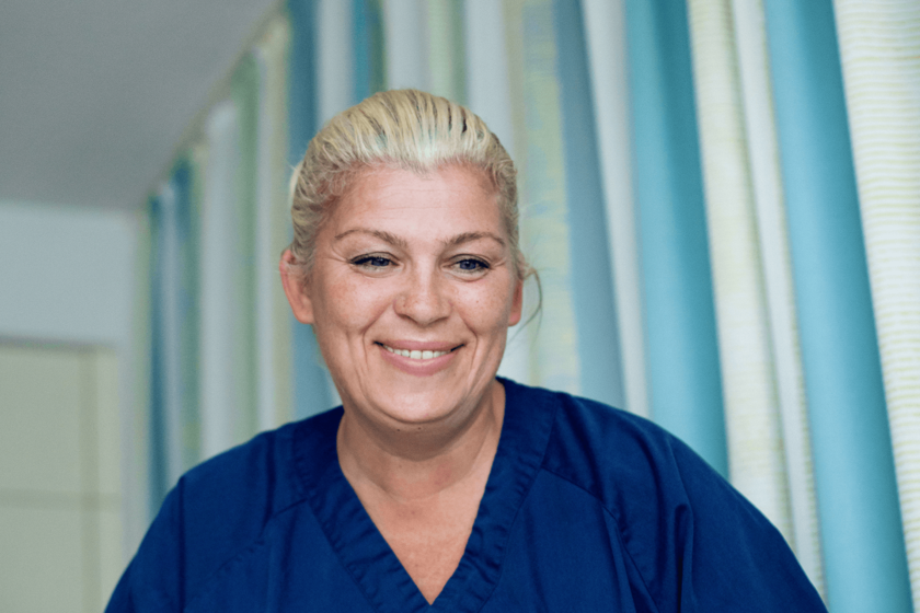 Kopf und Schultern einer lächelnden blonden Frau in einem dunkelblauen Oberteil