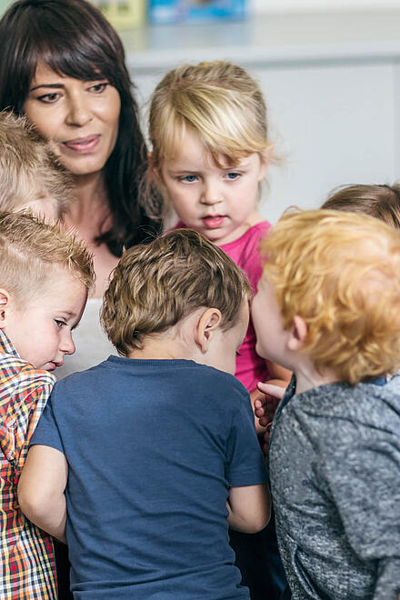 Eine Erzieherin umgeben von einer Gruppe Kindern.