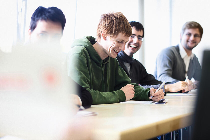 Studierende sitzen im Klassenraum und schreiben, unscharfer Vordergrund.