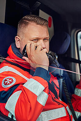 Johanniter in Einsatzkleidung im Rettungswagen, schaut aus dem Fenster und setzt einen Funkspruch ab