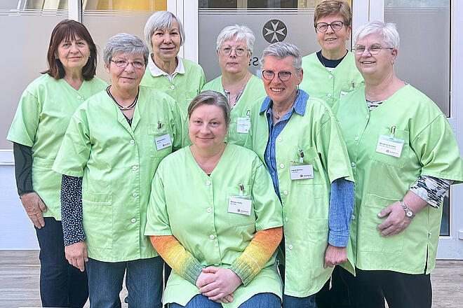 Gruppenbild von 8 älren Damen im typischen lindgrünen Kittel des Besuchsdienstes