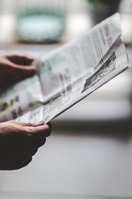Eine Person hält eine Zeitung in der Hand.