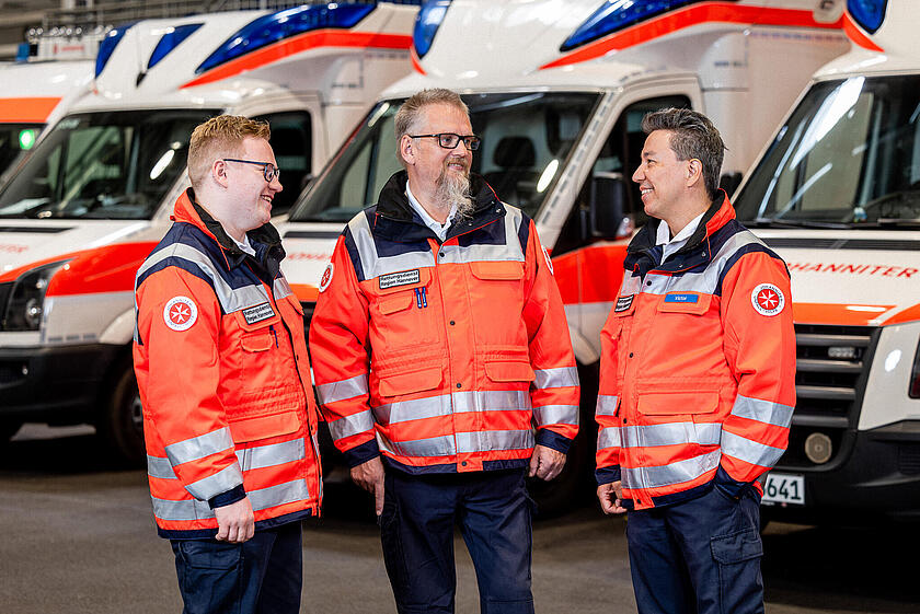 Drei Rettungsdienstmitarbeiter vor Rettungswagen in einer Halle